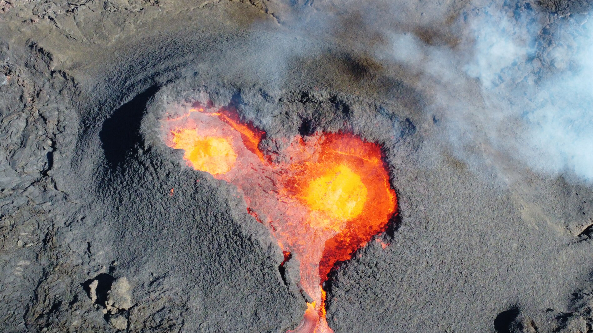 Aerial close-up of a heart-shaped molten lava pool ringed by black ash.