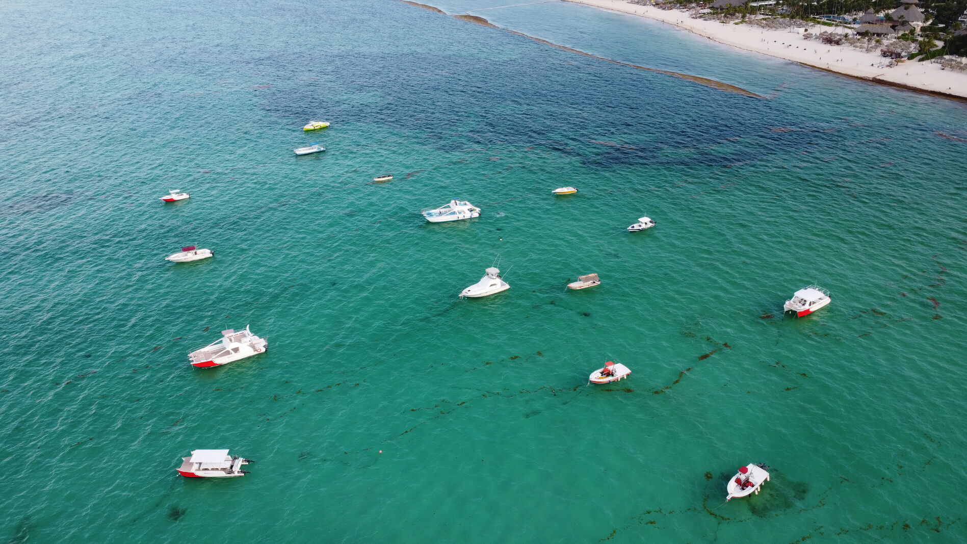 Anchored boats on saturated turquoise Caribbean water seen from above.