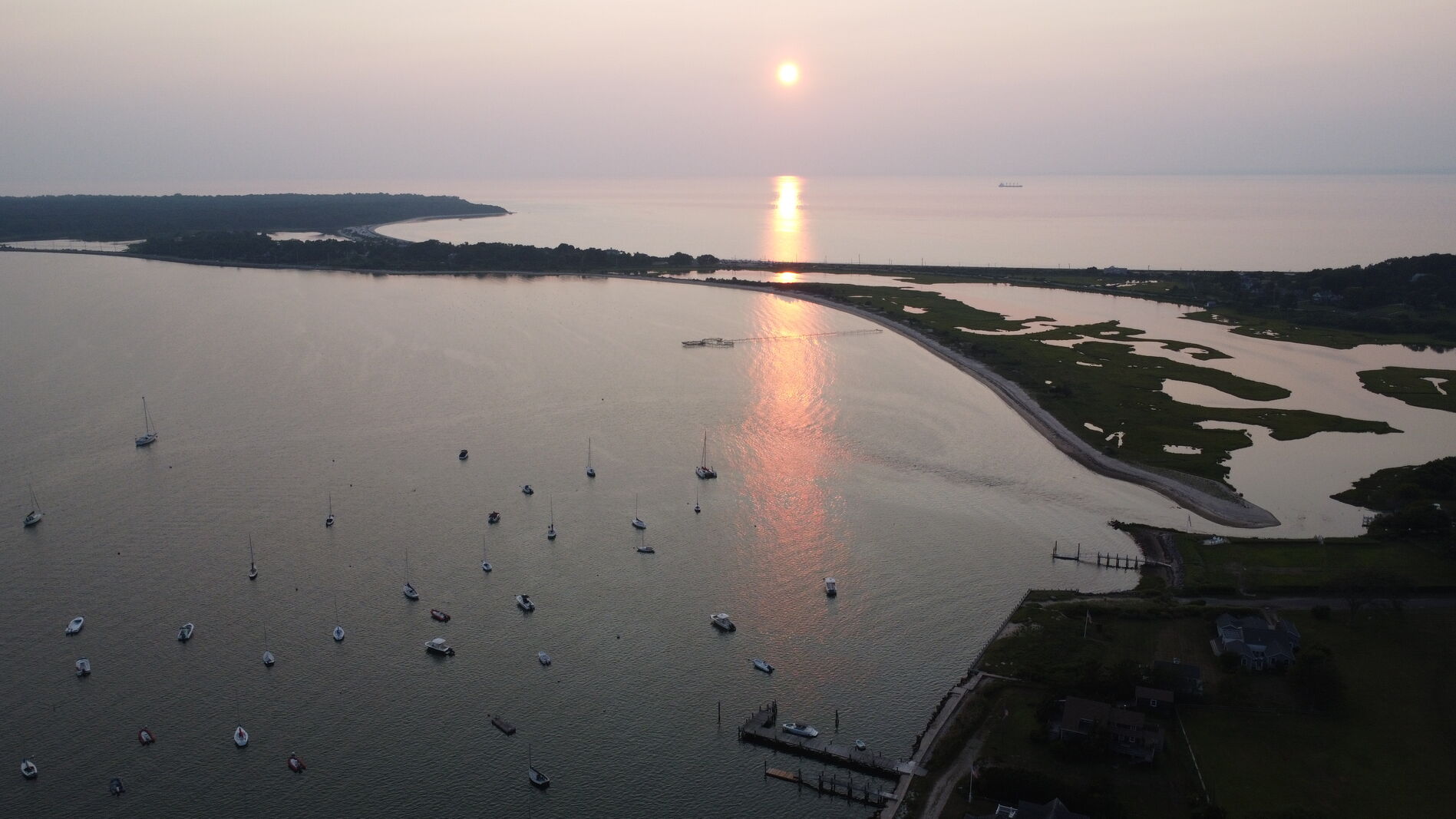 Sunset reflection column over a harbor full of sailboats.