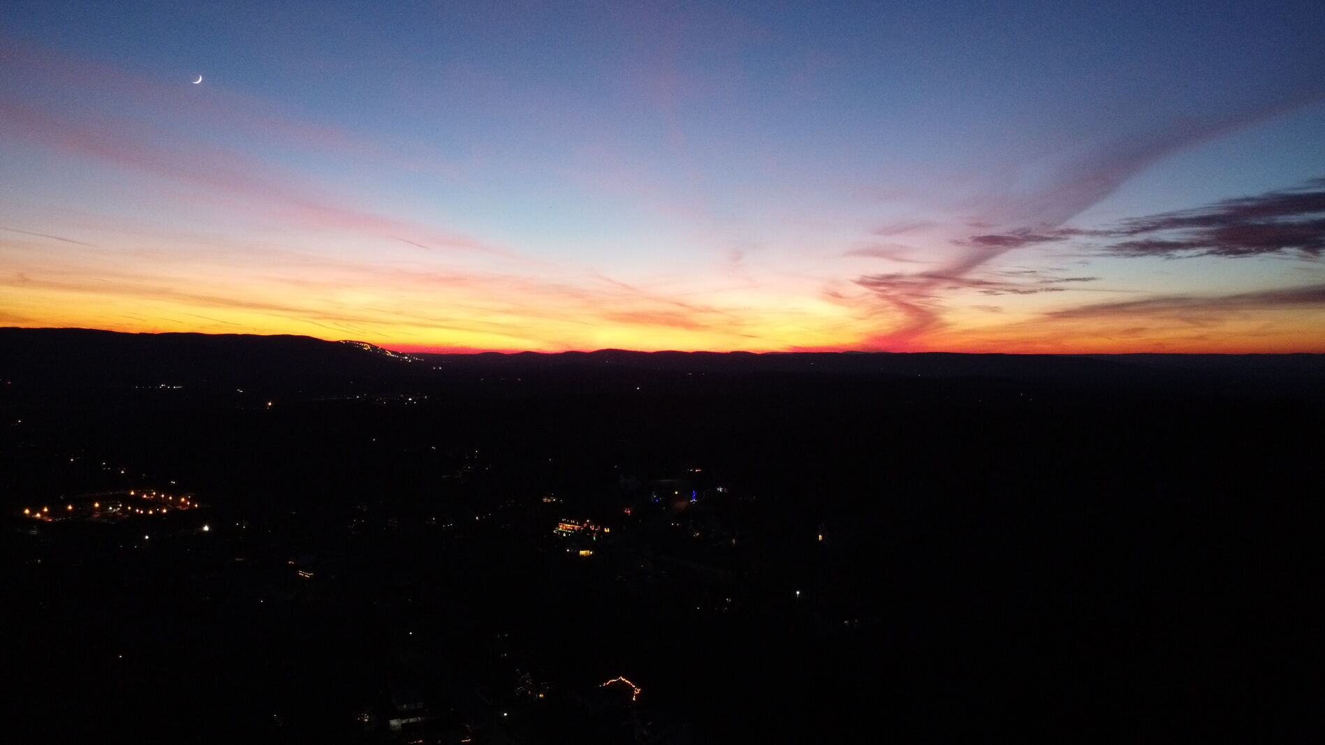 Blue-hour aerial sunset, deep teal sky over a glowing horizon ribbon.