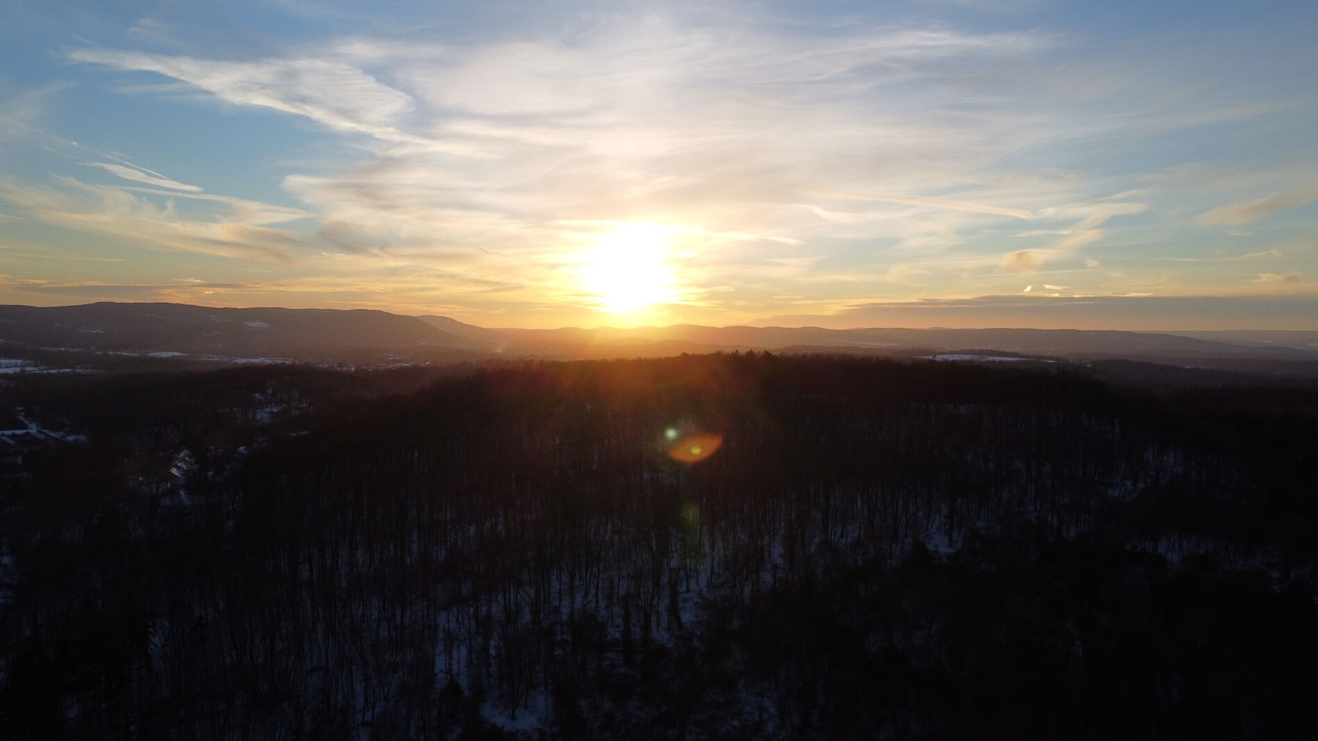 Golden hour sun cresting a snow-covered wooded ridge.