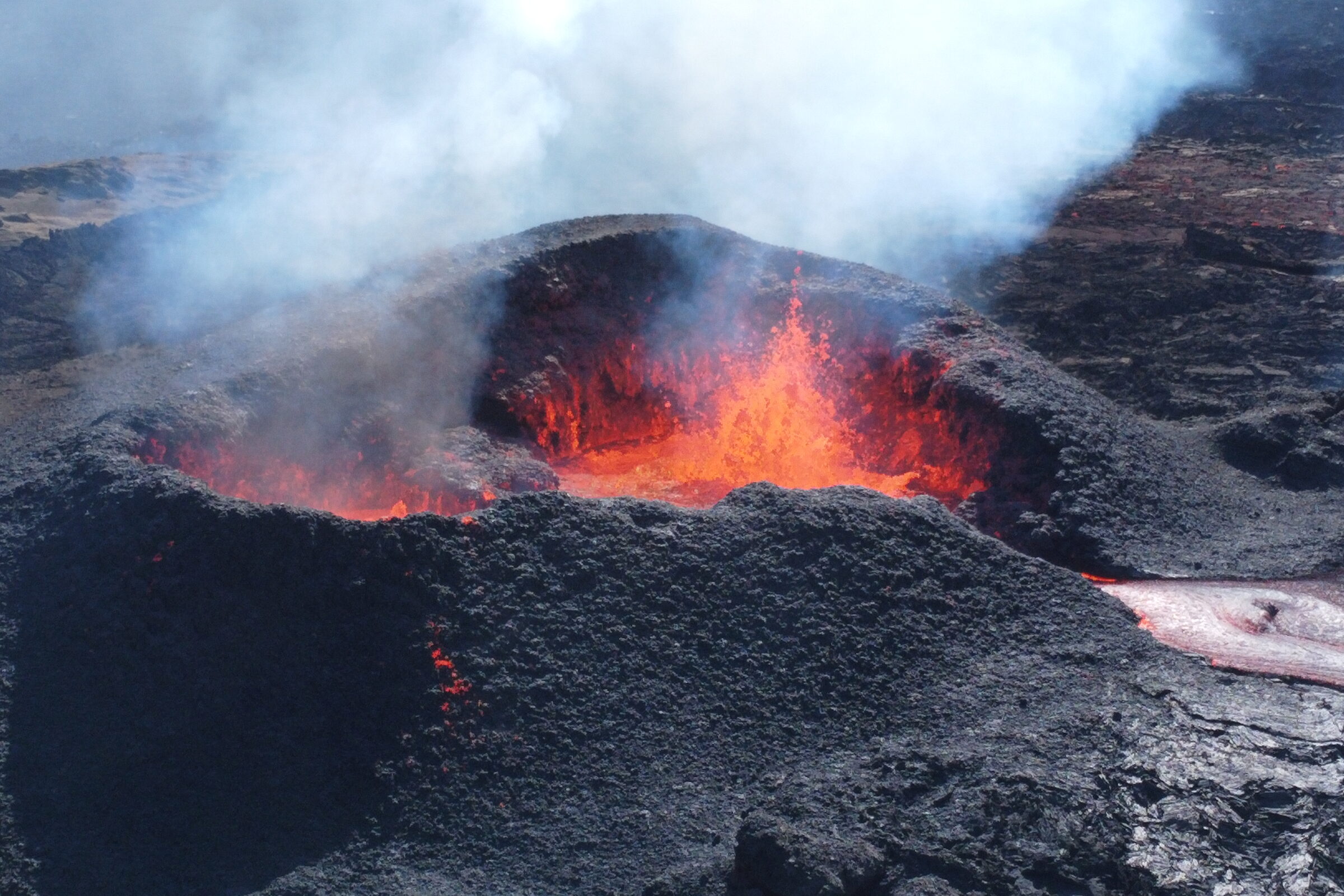 Aerial view of an active volcanic crater with molten lava and a rising steam plume.